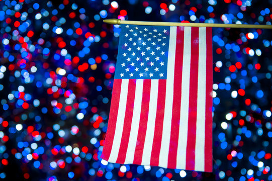 American flag hanging in front of celebratory bokeh background in red, white, and blue