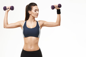 Sportive beautiful girl in sportswear training arms with dumbbells over white background.