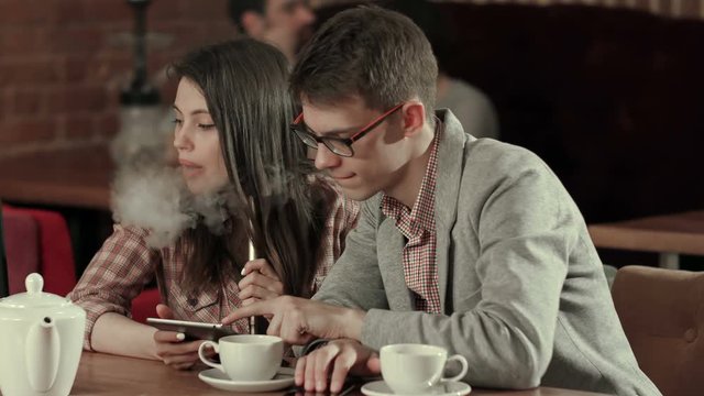 Girl using digital tablet and man smoking while looking at tablet