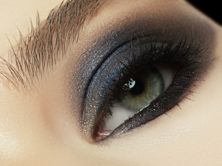 Close up of blue woman eye with beautiful brown with red and orange shades smokey eyes makeup....