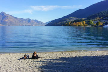 Two young women relaxing on the beach of Lake Wakatipu , Queenstown , South Island of New Zealand
