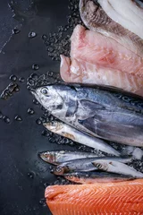 Foto auf Acrylglas Fish Vielzahl von rohem frischem Fisch. Ganzer Thunfisch und Hering, Lachsfilet, Kabeljau, roter Fisch auf zerkleinertem Eis auf dunklem, nassem Metallhintergrund. Draufsicht mit Platz. Fischmarktkonzept