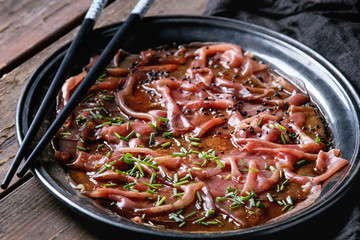 Asian style Beef carpaccio with soy sauce, chive onion, black sesame, served on vintage metal tray with textile napkin and chopsticks over old wooden plank background. Close up