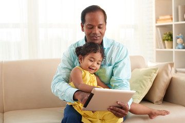 Cheerful middle-aged father and his pretty little daughter enjoying each others company while playing educational game on digital tablet - Powered by Adobe