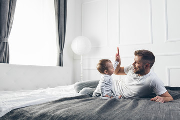 Happy father with his son playing at home on the bed - obrazy, fototapety, plakaty