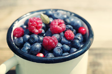 Berries of ripe juicy bilberry and raspberries in an old iron mug, close up