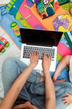 Close up photo of young mother working on laptop with her toddler child. Freelance business concept. Selective focus, top view