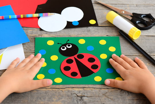 Child made a ladybird from colored paper. Summer card with paper ladybug, stationery on a wooden table. Simple paper circle crafts for teaching children to cut and glue. Development kids motor skills