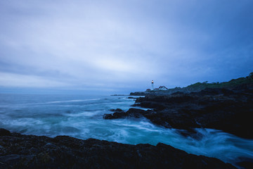 A lighthouse shines through dark clouds along the coast, Portland, Maine