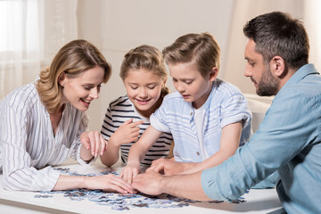 smiling family playing with puzzle on table at home together
