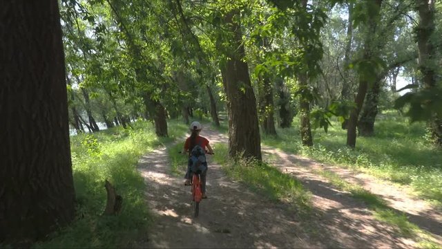 Child on a bicycle with a backpack. A girl is riding a bicycle in the forest.
