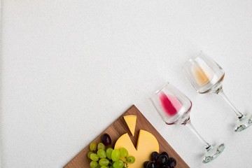 Two glasses of white and red wine, cheese and grapes. Top view