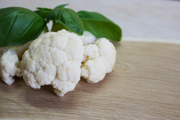 Fresh raw cauliflower and basil leaf on a wooden board. Selective focus. Close-up. Horizontal.