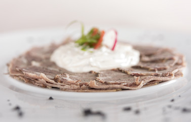 Beef carpaccio with mayonnaise, decorated with herbs, placed on white plate, light background,...