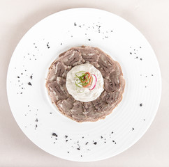 Beef carpaccio with mayonnaise, decorated with herbs, placed on white plate, light background, isolated