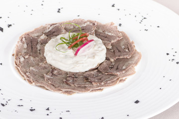 Beef carpaccio with mayonnaise, decorated with herbs, placed on white plate, light background, isolated
