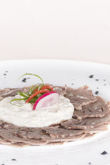 Beef carpaccio with mayonnaise, decorated with herbs, placed on white plate, light background, isolated