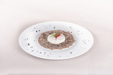 Beef carpaccio with mayonnaise, decorated with herbs, placed on white plate, light background, isolated