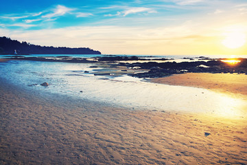 Coast of the sea at colorful sunset, Nang Thong Beach, Khao Lak, Thailand. Beach sunset is a golden sunset sky with a wave rolling to shore as the sun sets over the ocean horizon