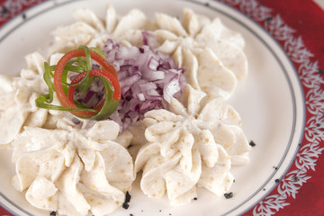 Fish roe salad, whit toasted bread, onion, green leafs, lemon, radish and olives, placed on a white plate, brown background