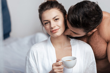 Portrait of young woman having coffee with boyfriend in bed
