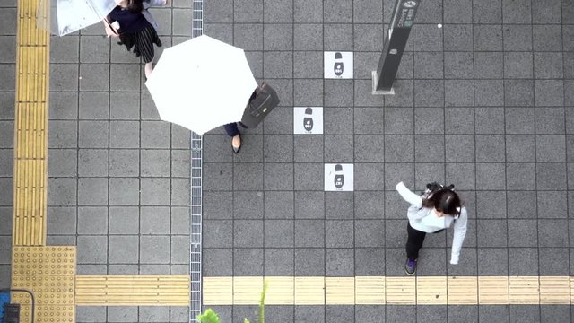 Female pedestrians walking holding umbrellas in slow motion in aerial view
