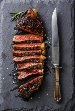 Sliced medium rare grilled Striploin steak and knife on slate board