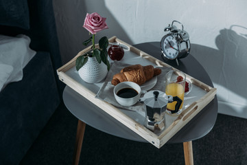 Tray with breakfast on table near bed in bedroom