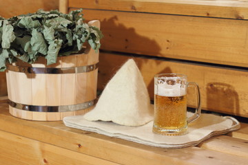 A mug of light beer and bath accessories are in the interior of the Russian bath.