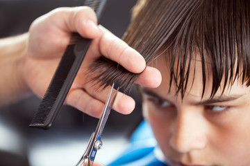 Dark haired boy at hairdresser while hairdressing by hairdresser