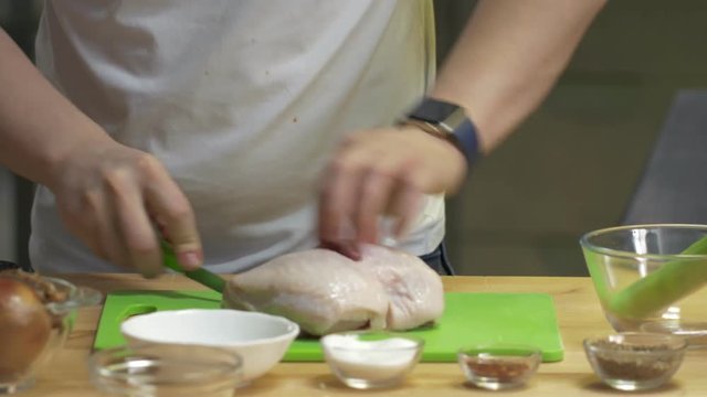 Hands of male chef carve chiken on a cutting boardand dips into boiling water on kitchen