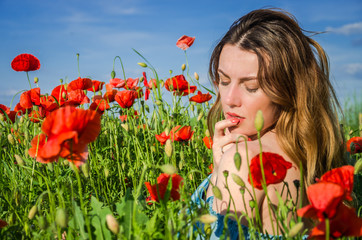 A young cheerful beautiful girl walks in a poppy meadow among red blooming poppies on a bright, hot, sunny summer day