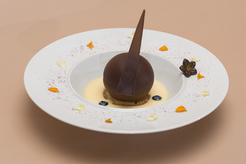 Luxurious dessert with chocolate globe and vanilla sauce, served on a biscuit, decorated with chocolate flower, flower petals and forest fruits, served in a white plate, light background, isolated