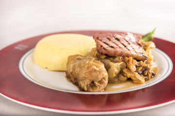 Sarmale, a traditional Romanian stuffed cabbage dish, served with polenta, bacon and hot chilli, placed on a white and red plate, light background