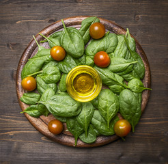 Healthy foods, cooking and vegetarian concept ingredients for the salad, fresh spinach leaves, cherry tomatoes, oil, laid out on a wooden cutting board