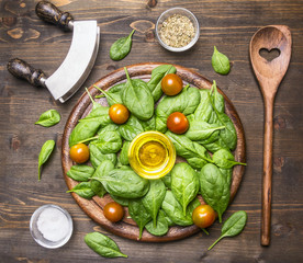 Superfoods and health or detox diet food concept Fresh spinach is laid out with a frame around the cutting board with a knife for salad, a wooden spoon, cherry tomatoes and spices