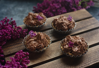 Homemade vanilla cupcake with chocolate frosting on wooden wooden background with lilac, selective focus. Delicious dessert for birthday, festive seasons, engagement or valentine day