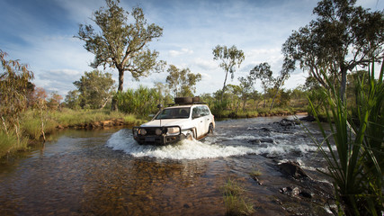 Obraz na płótnie Canvas A Four wheel drive vehicle crosses a flowing creek in the far North Kimberley of Western Australia on the road to Mitchell Plateau.