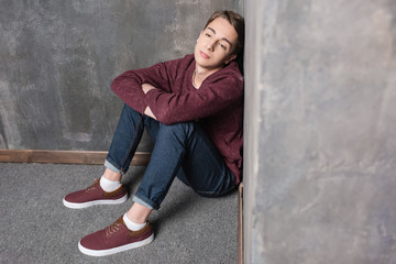 Depressed teenage boy sitting on floor and looking away