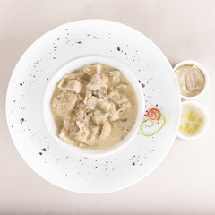 Tripe soup, served with garlic sauce – “mujdei” and horseradish sauce, decorated with green and red leafs, placed on white plate, light background, isolated