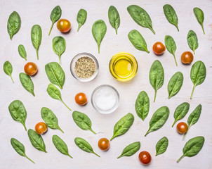 Healthy foods, cooking and vegetarian concept  fresh spinach leaves are laid out around the condiments and oil, top view, on a rustic wooden background
