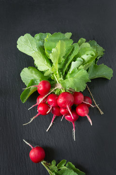 Ripe bunch organic red radish with foliage on a black slate dish as background. Top view.