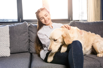 teenager girl hugging golden retriever dog on sofa at home