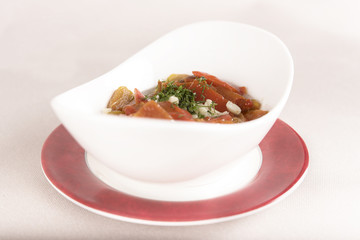 Roasted bell pepper salad with green herbs, place in a white bowl, on a red and white plate, light background, isolated