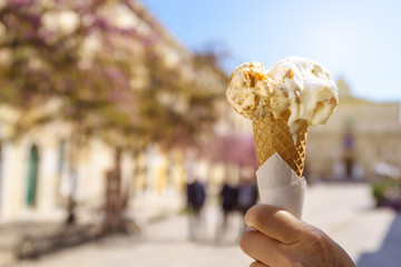 Close up of female hand holding melting delicious ice cream gelato cone with warm sun flare in summer, Italy