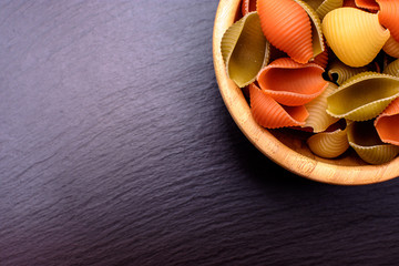 Colored pasta lie in a wooden cup on a black stone slate, place for text