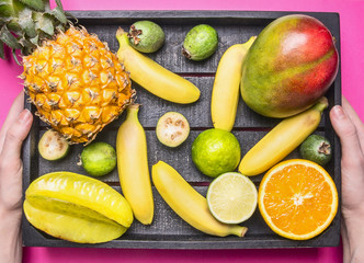 fresh summer fruit mix, mini pineapple, mango, mini bananas, carambola, lime, quince in a wooden box that holds the girl, top view