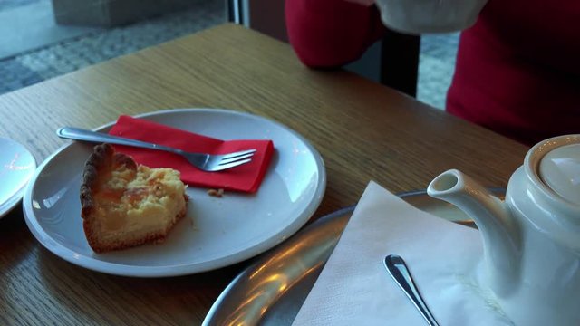 A woman sits at a table with meal in a cafe, drinks tea, refills the cup and drinks again - closeup on the table from above