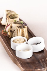 Bone marrow served with garlic, horseradish puree and black, pink and white salt, place on a wooden board, decorated with radish and fresh leafs, light background, isolated