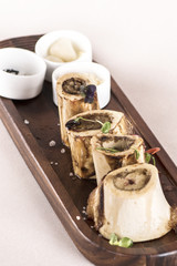 Bone marrow served with garlic, horseradish puree and black, pink and white salt, place on a wooden board, decorated with radish and fresh leafs, light background, isolated